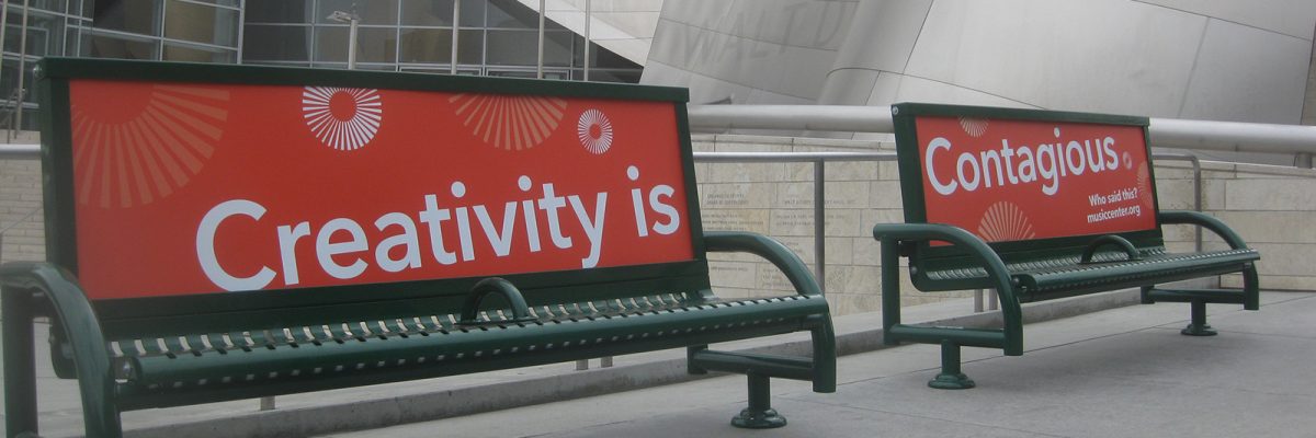 Two benches in front of Walt Disney Concert Hall, Los Angeles, with signage on backrests reading 'Creativity is' and 'Contagious'